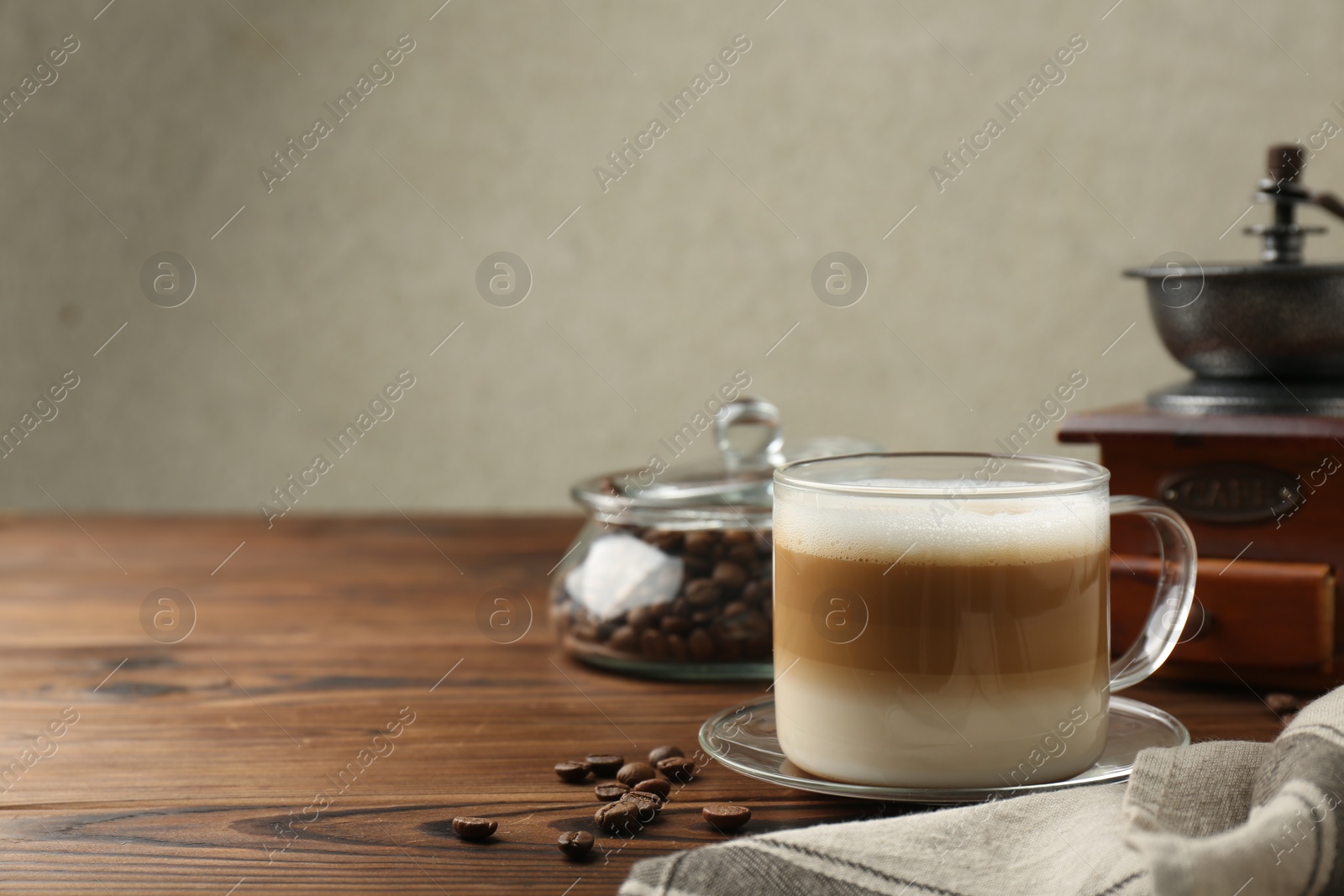 Photo of Aromatic coffee in cup, beans and manual grinder on wooden table, space for text