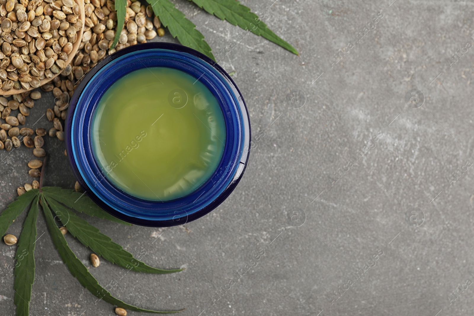 Photo of Jar of hemp cream and seeds on grey stone table, flat lay with space for text. Organic cosmetics