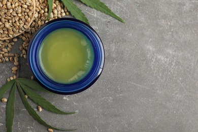 Photo of Jar of hemp cream and seeds on grey stone table, flat lay with space for text. Organic cosmetics