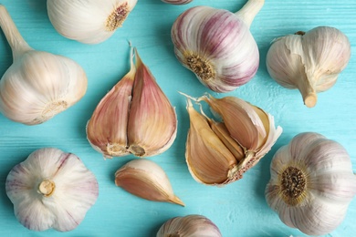 Photo of Fresh unpeeled garlic bulbs and cloves on light blue wooden table, flat lay. Organic product