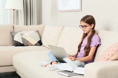 Girl with laptop and books on sofa at home