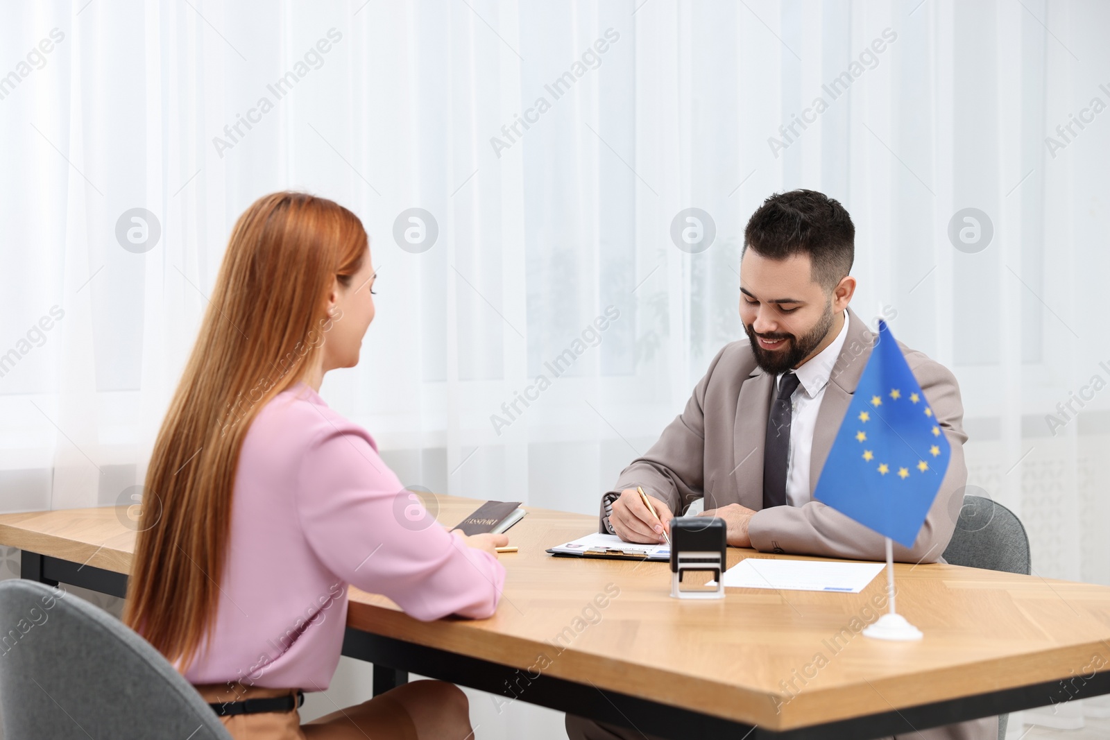 Photo of Immigration to European Union. Embassy worker approving visa application form to woman in office