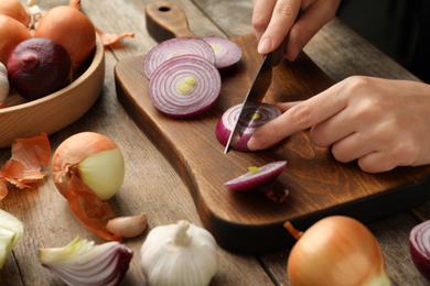 Photo of Woman cutting red onion on wooden board, closeup