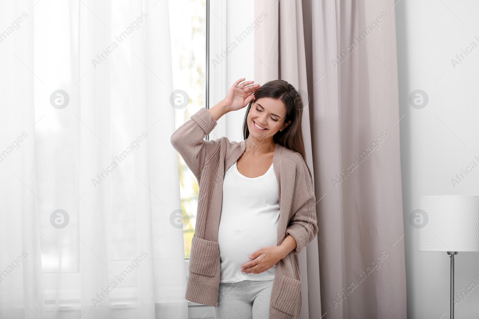 Photo of Happy pregnant woman standing near window at home