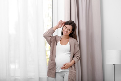 Happy pregnant woman standing near window at home