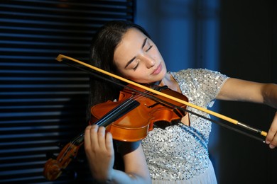 Photo of Beautiful young woman playing violin in dark room