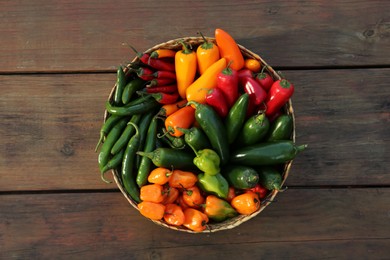 Photo of Wicker basket with many different fresh chilli peppers on wooden table, top view