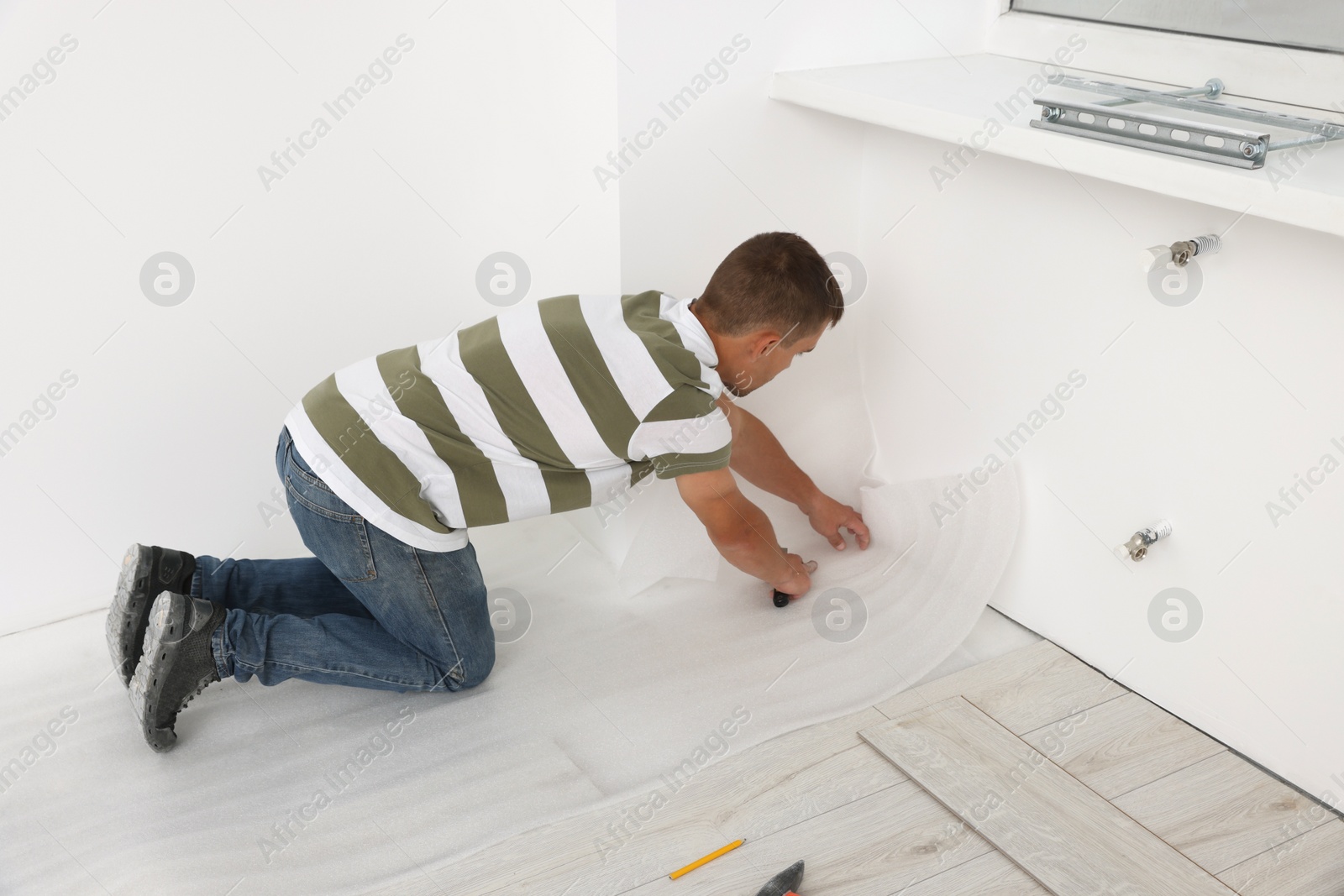 Photo of Professional worker cutting polyethylene foam during installation of laminate flooring indoors