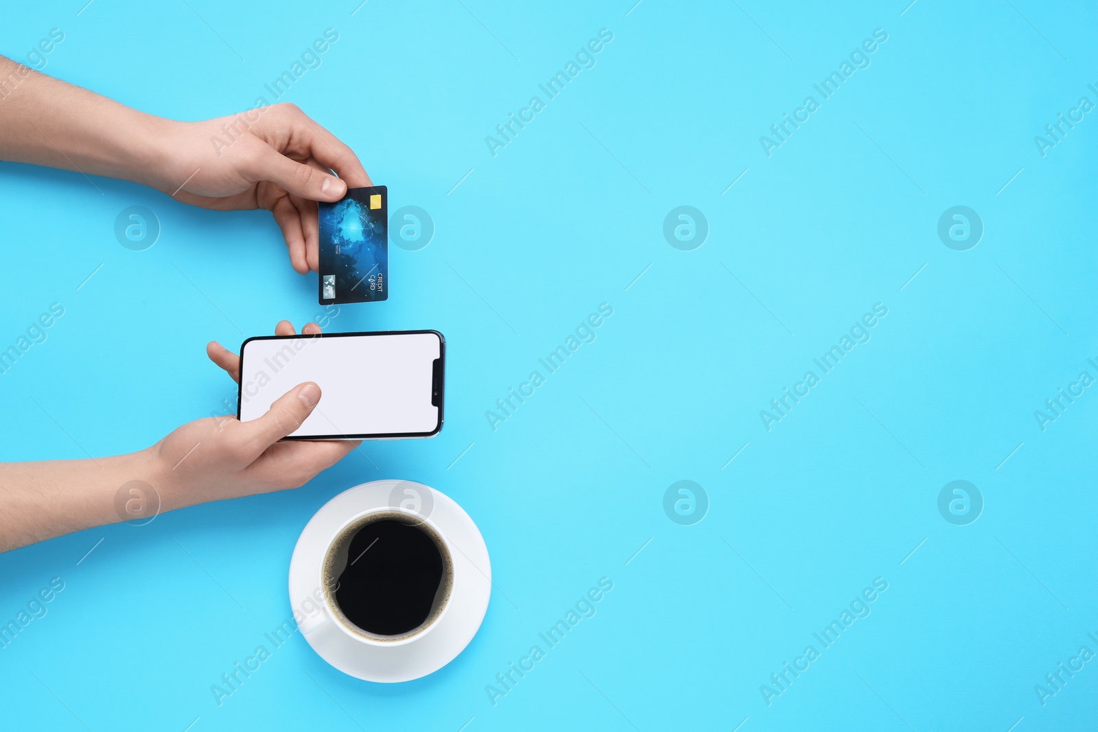 Photo of Online payment. Man with smartphone, credit card and coffee on light blue background, top view. Space for text