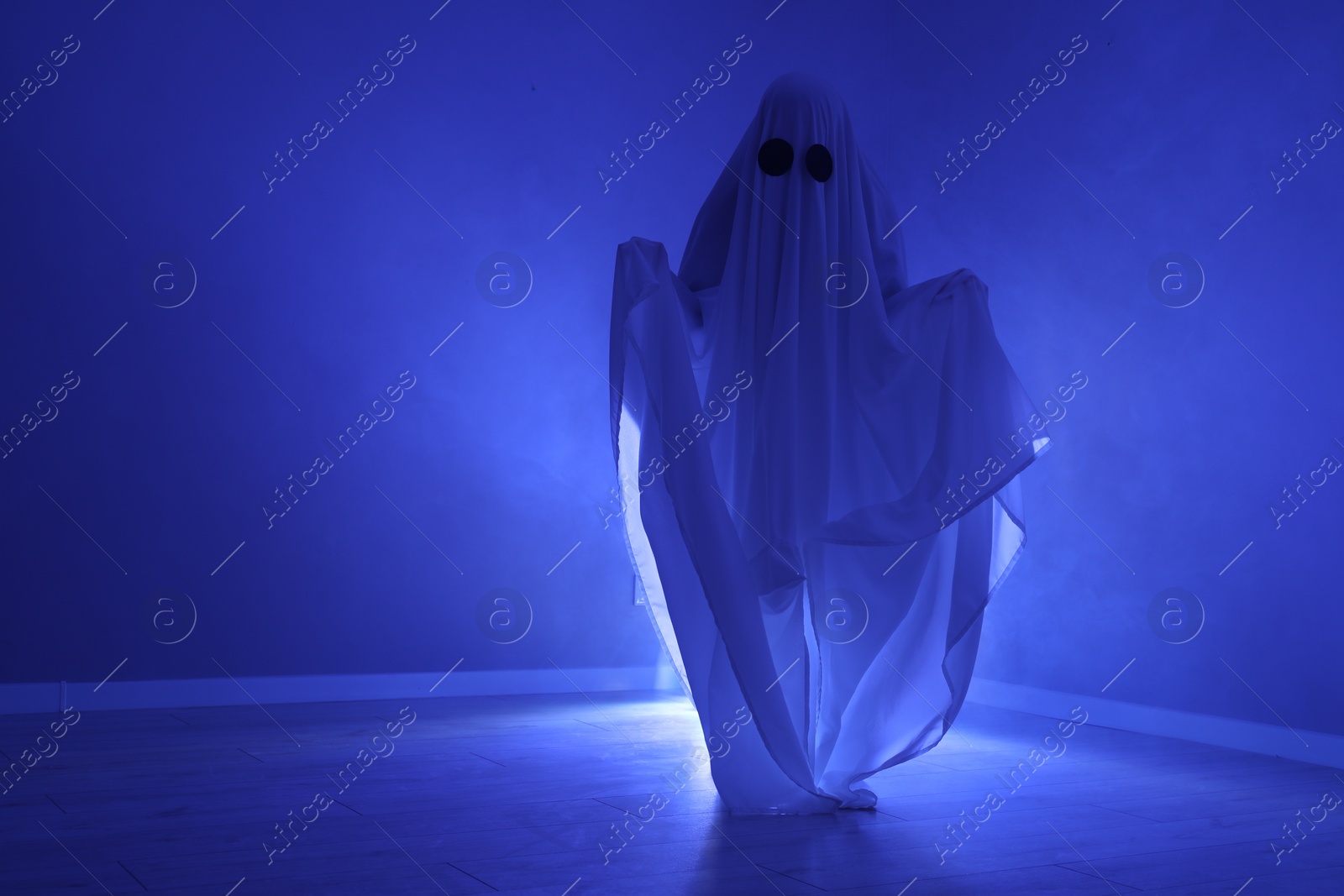 Photo of Creepy ghost. Woman covered with sheet in blue light, space for text