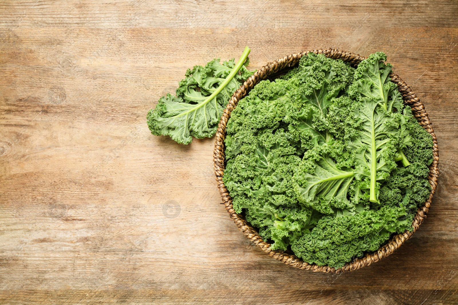 Photo of Fresh kale leaves on wooden table, top view. Space for text