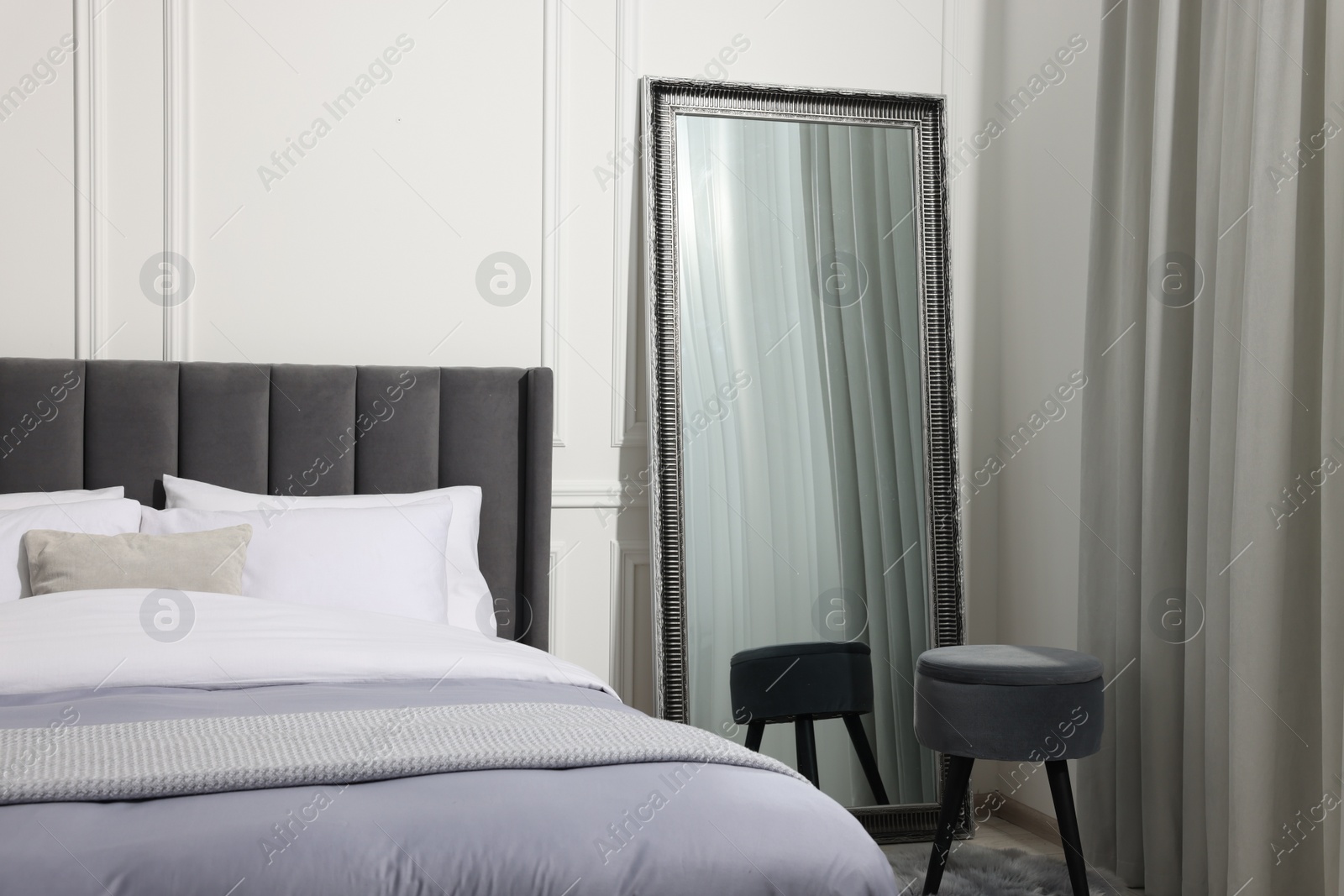 Photo of Cozy bed, mirror and pouf in stylish bedroom