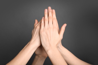 Photo of Group of young people giving high five on grey background, closeup. Victory concept