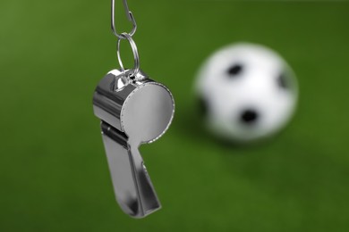 Football referee equipment. Metal whistle on blurred green background, closeup with space for text