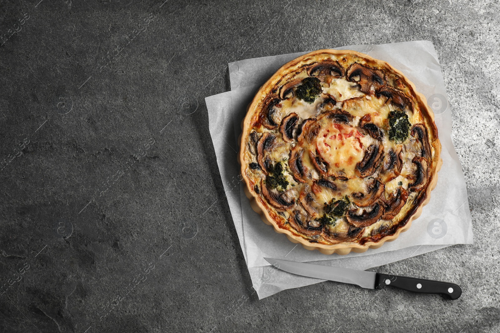 Photo of Delicious quiche with mushrooms and knife on dark grey table, flat lay. Space for text