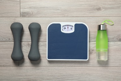 Photo of Scales, dumbbells and sport bottle on wooden background, top view. Weight loss
