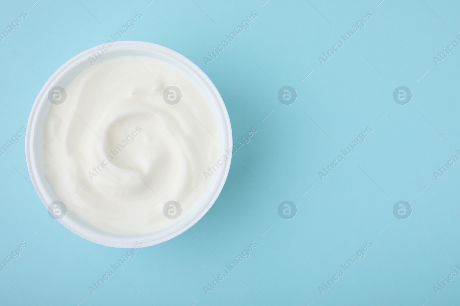 Photo of Delicious natural yogurt in plastic cup on light blue background, top view. Space for text