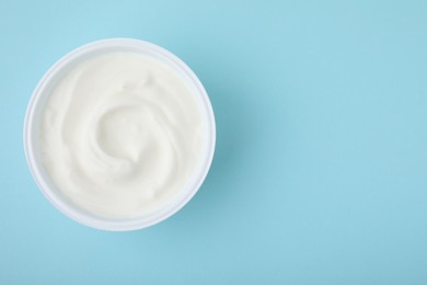 Photo of Delicious natural yogurt in plastic cup on light blue background, top view. Space for text