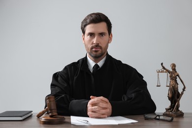 Judge with gavel and papers sitting at wooden table against light grey background