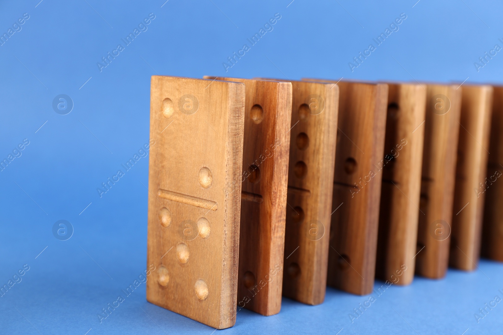 Photo of Row of wooden domino tiles on blue background, closeup