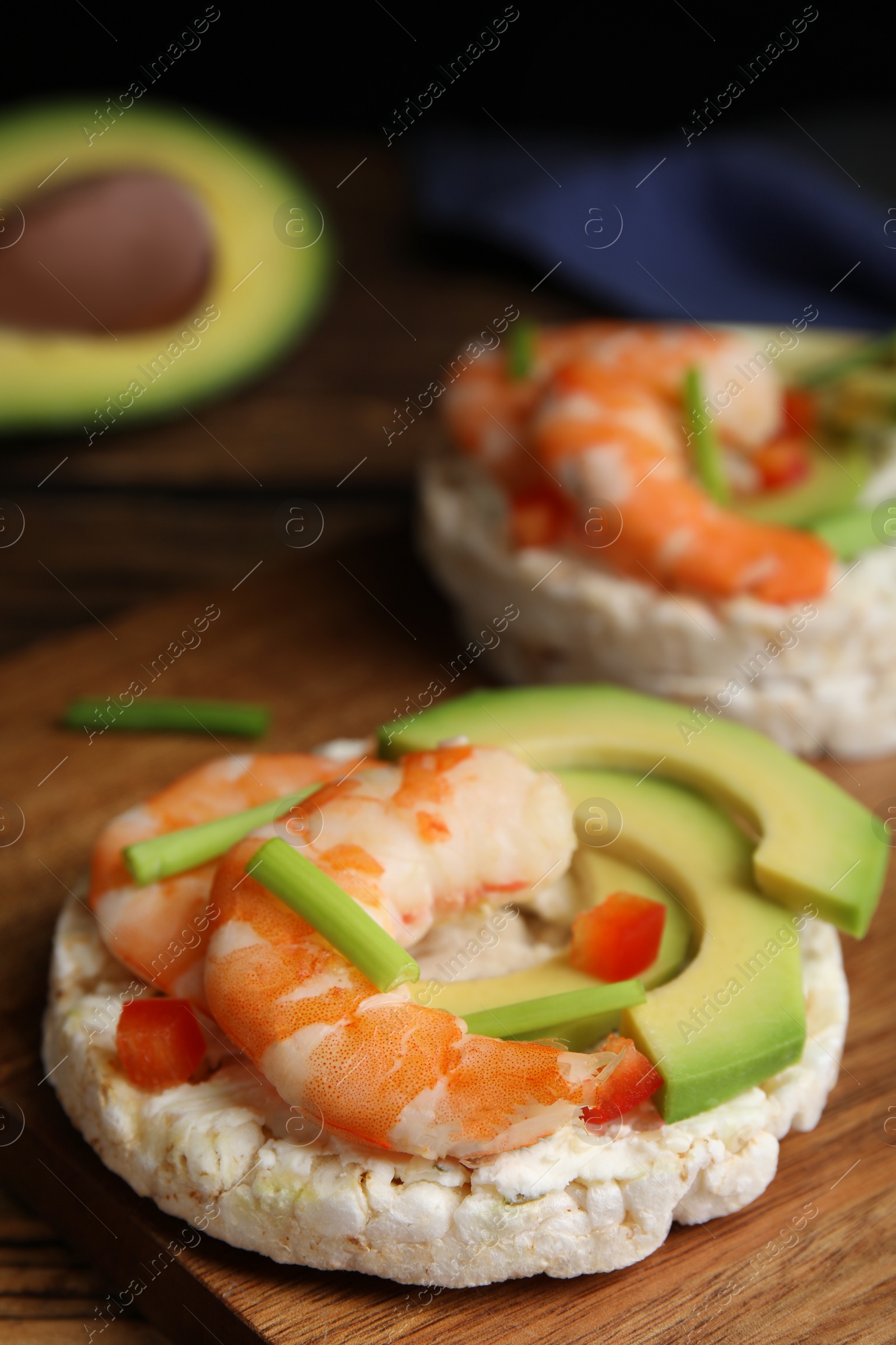 Photo of Puffed rice cakes with shrimps and avocado on wooden board, closeup