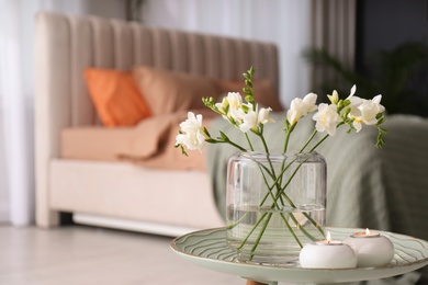 Photo of Vase with beautiful freesia flowers and burning candles on stand in bedroom, space for text. Interior elements