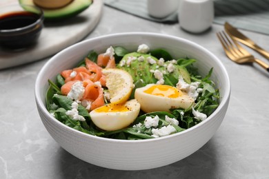 Delicious salad with boiled egg, salmon and cheese in bowl on light grey marble table, closeup