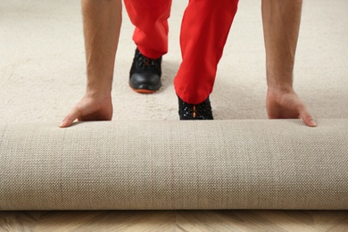 Photo of Worker rolling out new carpet flooring indoors, closeup