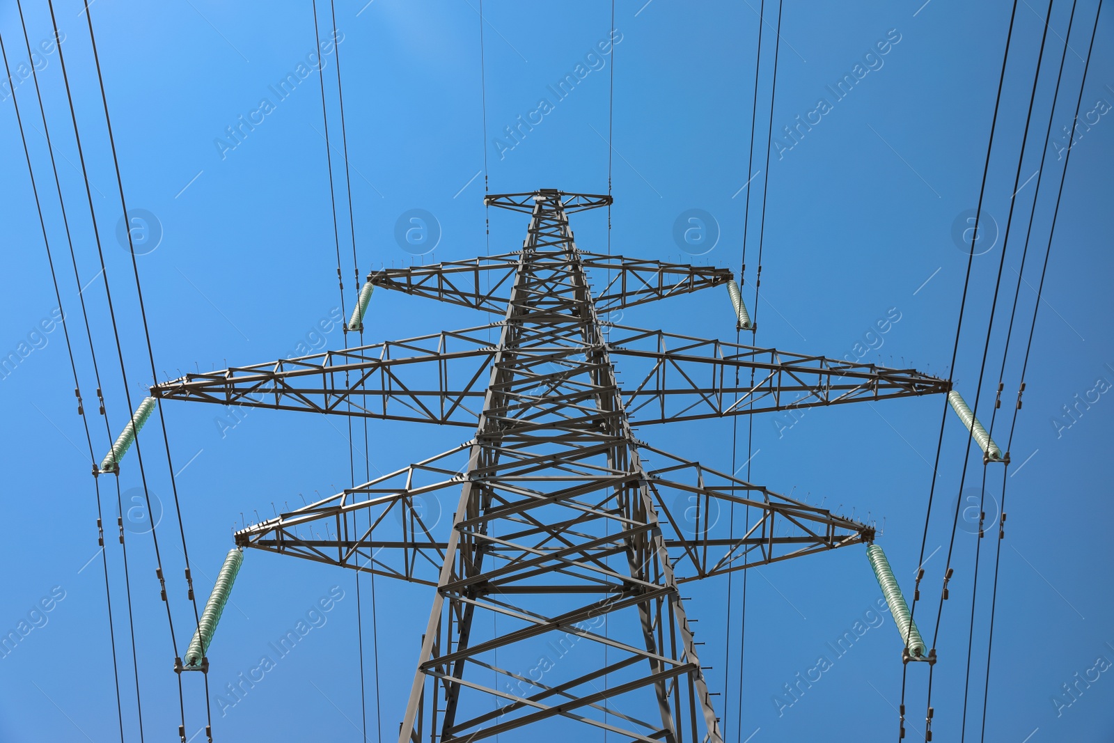 Photo of High voltage tower with electricity transmission power lines against blue sky, low angle view