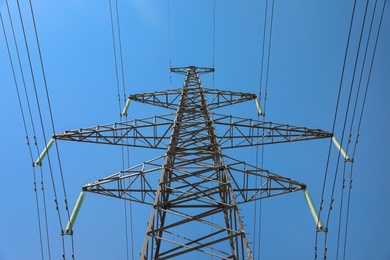 High voltage tower with electricity transmission power lines against blue sky, low angle view