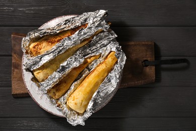 Photo of Tasty baked parsnips on black wooden table, top view