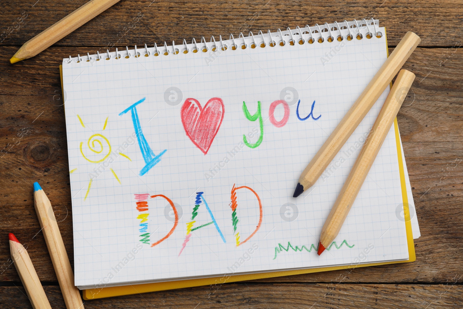 Photo of Notebook with words I LOVE YOU DAD and pencils on wooden table, flat lay