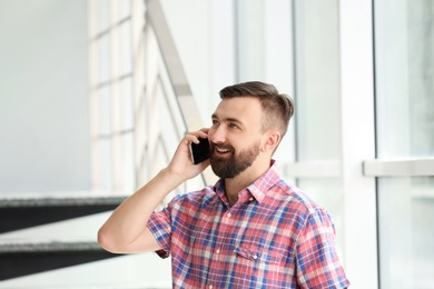 Photo of Portrait of handsome bearded man with mobile phone near stairs, indoors