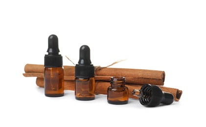 Photo of Bottles with cinnamon oil and sticks on white background