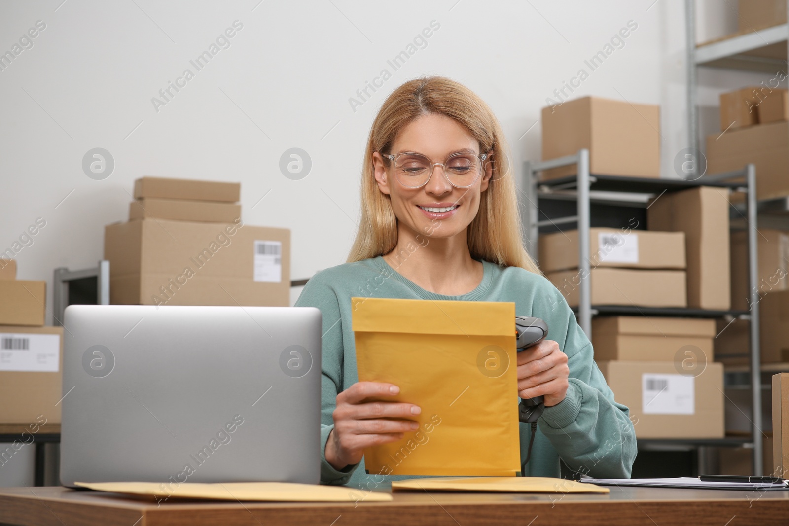 Photo of Seller with scanner reading parcel barcode at table in office. Online store