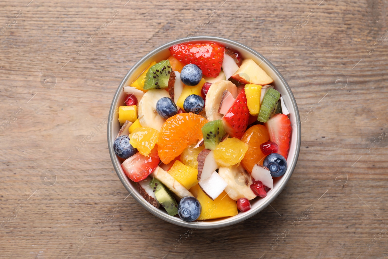 Photo of Delicious fresh fruit salad in bowl on wooden table, top view