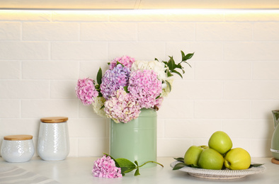 Photo of Beautiful hydrangea flowers and apples on light countertop