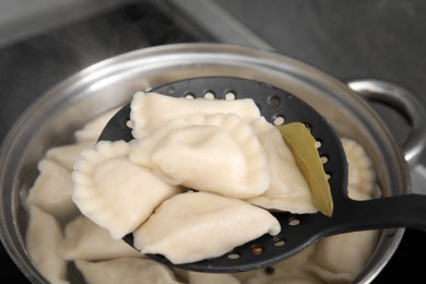 Photo of Dumplings (varenyky) with tasty filling on skimmer over pot indoors, closeup