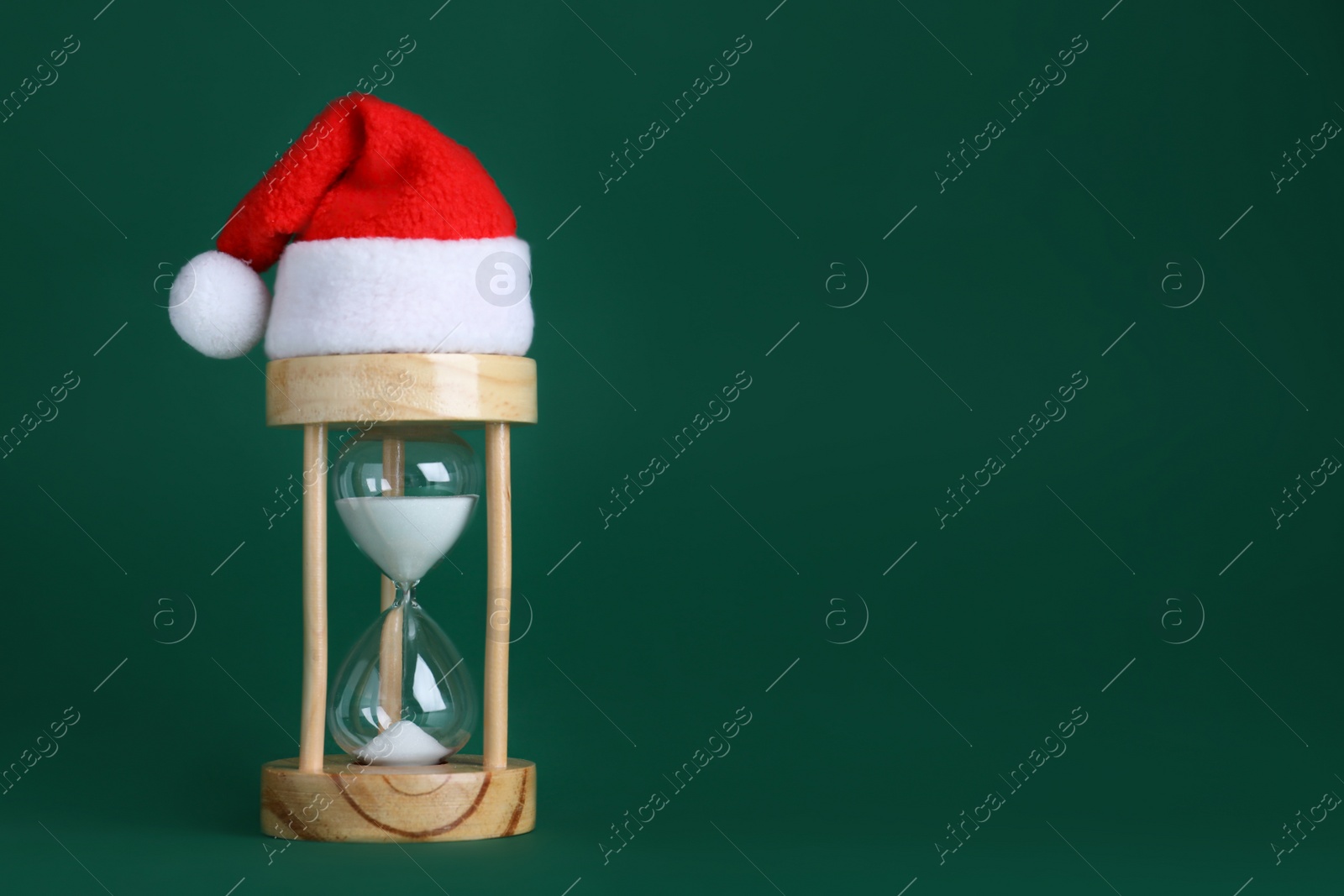 Photo of Hourglass and Santa hat on green background, space for text. Christmas countdown