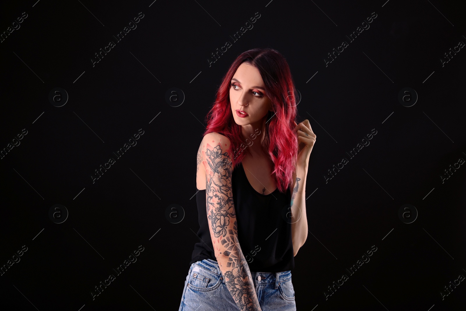 Photo of Beautiful woman with tattoos on arms against black background