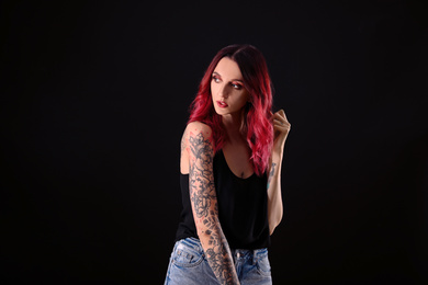 Beautiful woman with tattoos on arms against black background