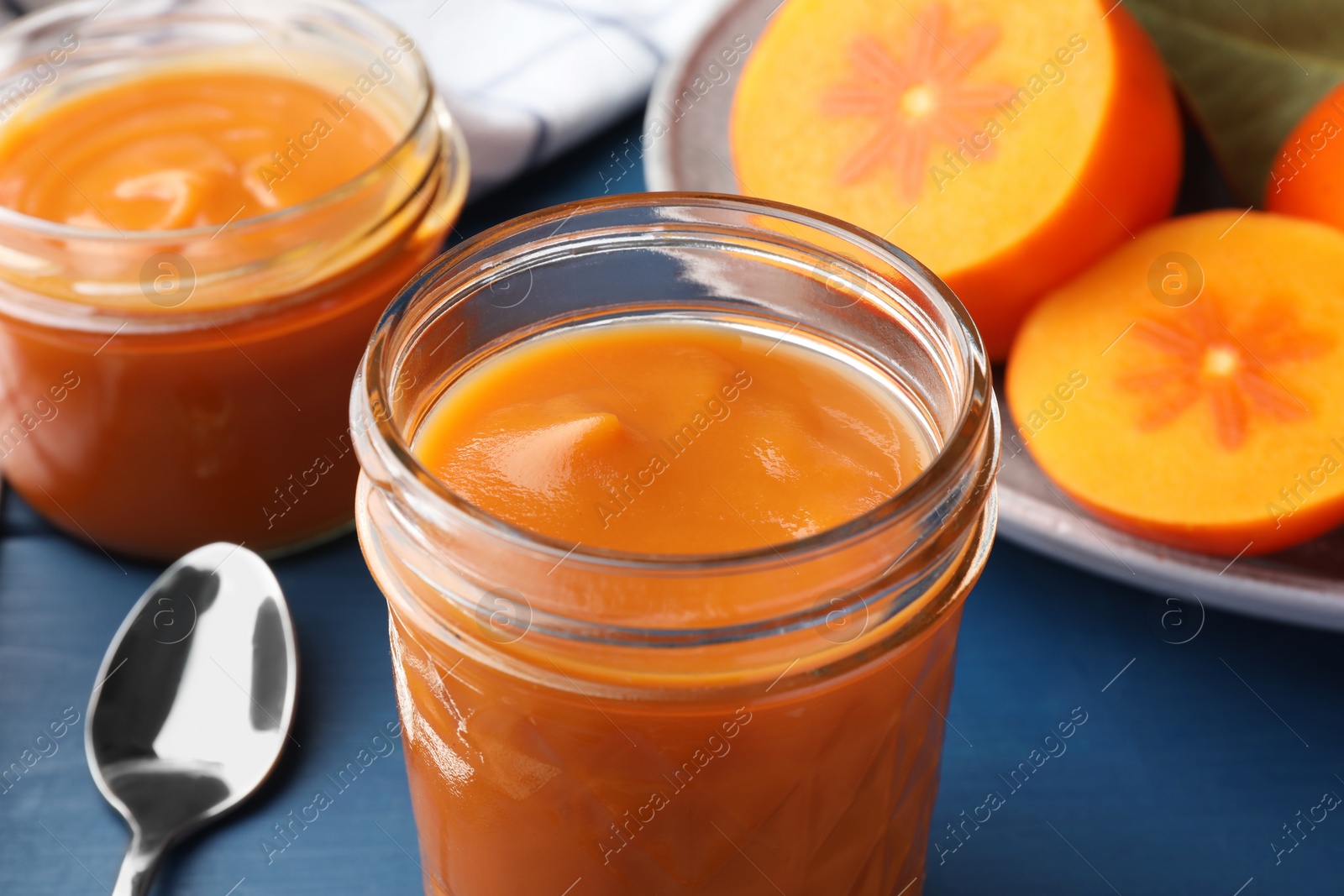 Photo of Delicious persimmon jam in glass jars served on blue table, closeup