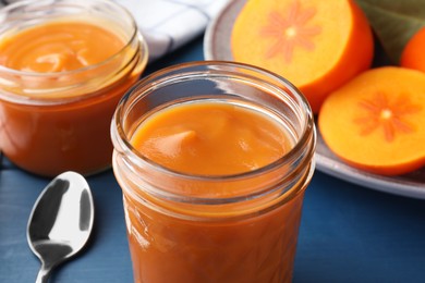 Photo of Delicious persimmon jam in glass jars served on blue table, closeup