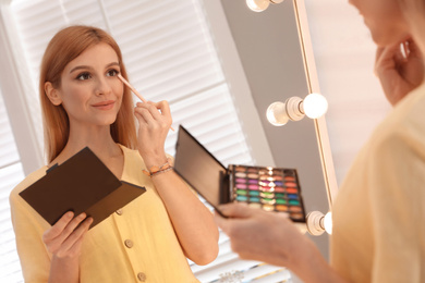 Beautiful young woman applying makeup near mirror in dressing room