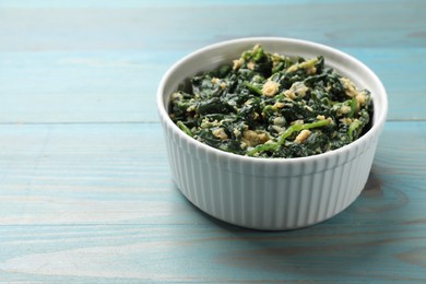 Photo of Tasty spinach dip with egg in bowl on light blue wooden table, closeup. Space for text