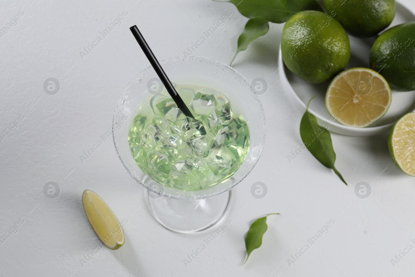 Photo of Delicious Margarita cocktail with ice cubes in glass and lime on white table