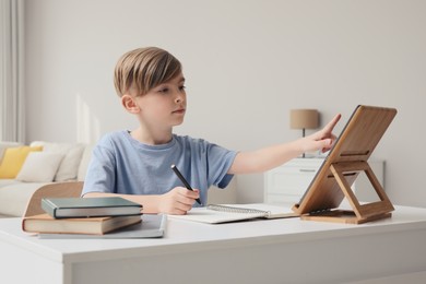 Photo of Boy doing homework with tablet at table indoors