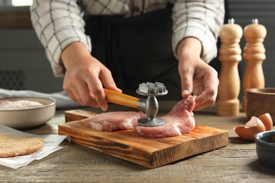 Photo of Woman cooking schnitzel at wooden table, closeup