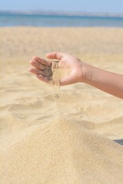 Photo of Child pouring sand from hand on beach, closeup. Fleeting time concept