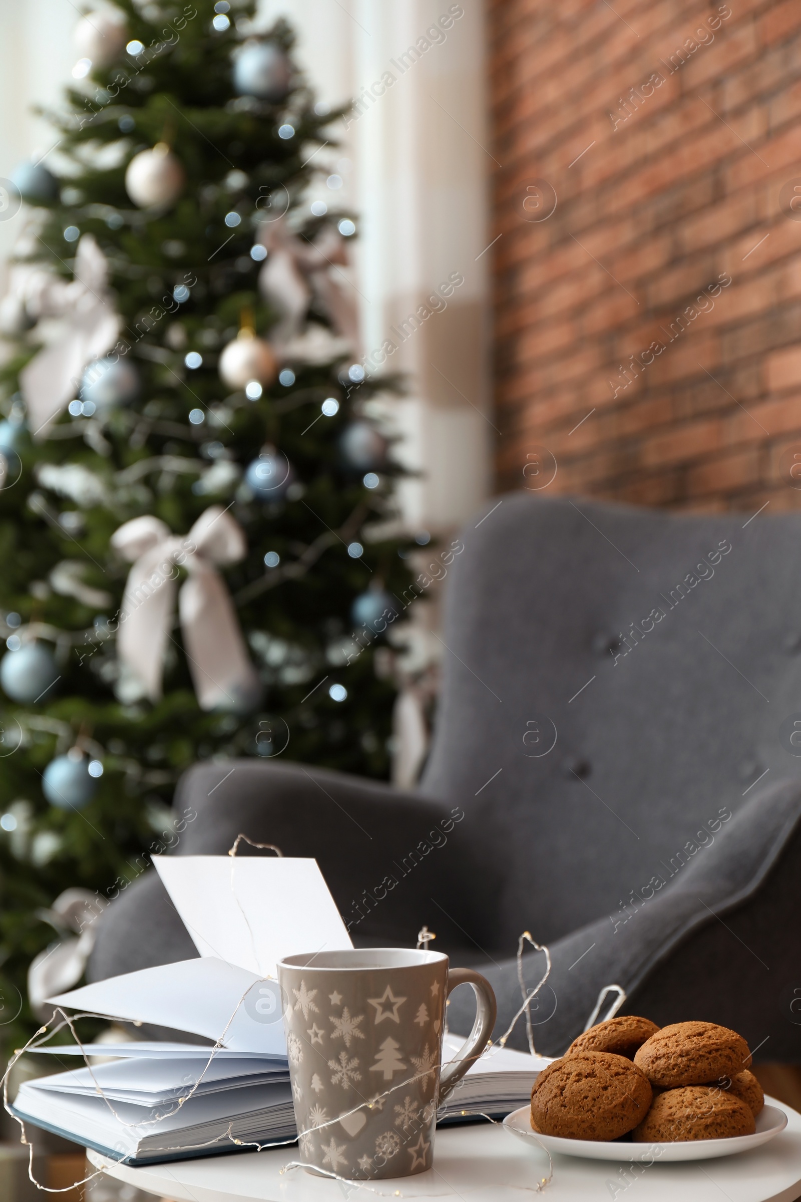 Photo of Book with treat on table and Christmas tree in stylish living room interior